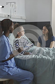 Nurse consulting sick hospitalized little daughter resting in pediatric healthcare clinic