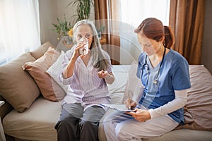 Nurse cosulting with senior her health condition, taking pills.