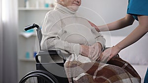 Nurse covering old woman in wheelchair with blanket, taking care about patient