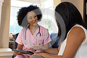 Nurse with curly hair showing tablet to patient at home photo