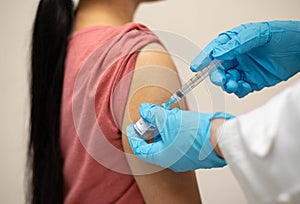 Nurse, doctor or General practitioner in blue gloves holding syringe, making injection or vaccination to young female patient in