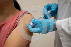 Nurse, doctor or General practitioner in blue gloves holding syringe, making injection or vaccination to young female patient in