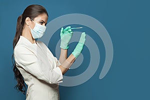 Nurse or doctorwoman wearing professional medical uniform and protective face mask holding syringe on blue background. Medicine,