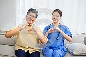 Nurse with elderly patient showing hand heart showing health improvement from treatment in room.Health care concept