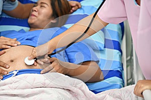 Nurse examining pregnant woman with stethoscope at maternity ward