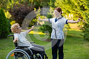 A nurse is exercising with an elderly patient in a wheelchair outdoors.