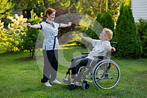 A nurse is exercising with an elderly patient in a wheelchair outdoors.