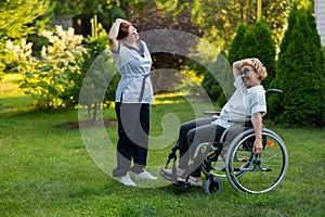 A nurse is exercising with an elderly patient in a wheelchair outdoors.