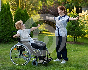 A nurse is exercising with an elderly patient in a wheelchair outdoors.