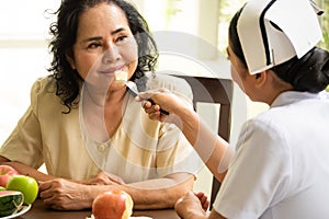 Nurse giving apple to senior female patient in the room