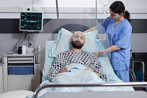 Nurse fixing pillow taking care of patient with respiratory insufficiency connected to vitals monitor