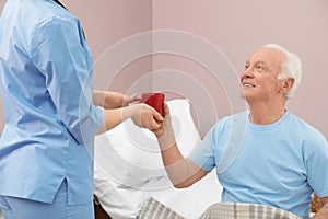 Nurse giving drink to senior man in hospital ward