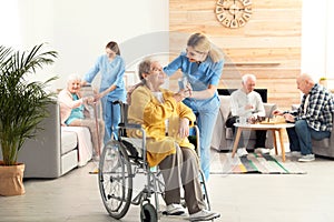 Nurse giving glass of water to elderly woman in wheelchair. Assisting senior people