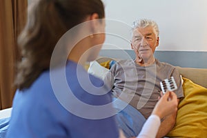 Nurse giving pills senior man in his home.