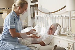 Nurse Giving Senior Male Medication In Bed At Home