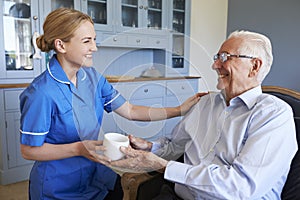 Nurse Giving Senior Man Cup Of Tea On Home Visit