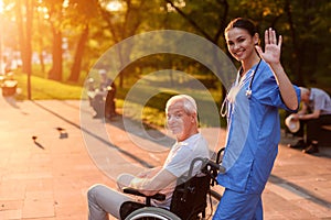 A nurse is greeting someone. Behind her in the wheelchair sits an old man and smiles