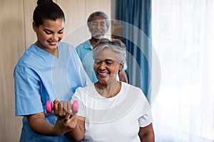 Nurse guiding senior woman in lifting dumbbell