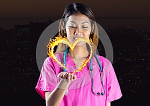 nurse with hand spread of with heart fire icon over in front of the city at night.