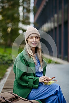 Nurse having healthy snack in front of hospital building, taking break from work. Importance of breaks in healthcare.