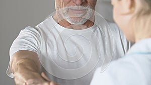 Nurse helping elderly man to lift his hand with dumbbell, rehab after surgery