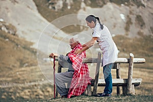 Nurse helping elderly senior man to walk on frash air