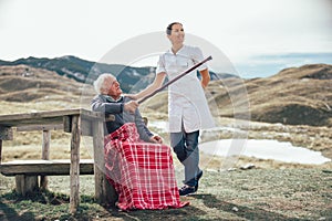 Nurse helping elderly senior man to walk on frash air