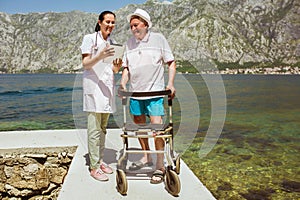 They are using digital tablet. Senior man using a walker with caregiver near the sea at summer