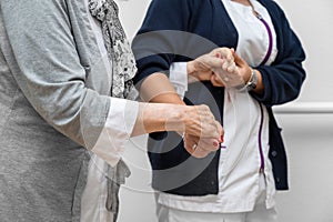 Nurse helping elderly woman walk in the room, holding his hand, supporting her. Treatment and rehabilitation after