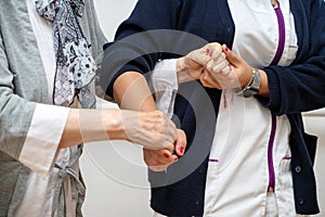 Nurse helping elderly woman walk in the room, holding his hand, supporting her. Treatment and rehabilitation after