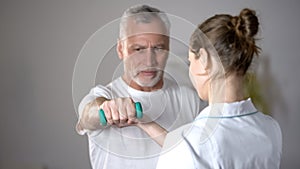 Nurse helping old man to lift dumbbell, cardiac rehabilitation, injury recovery