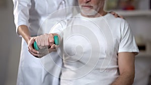 Nurse helping pensioner to lift dumbbell, rehabilitation center after insult