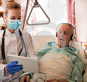 Nurse helping senior man in hospital to make conference call with family