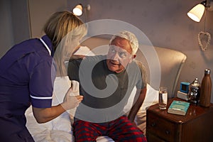 Nurse Helping Senior Man Out Of Bed On Home Visit