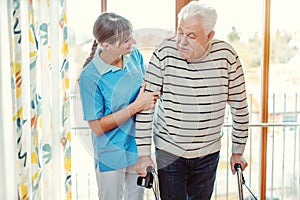 Nurse helping senior man with walking frame in nursing home