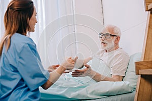 Nurse helping senior patient in bed to hold