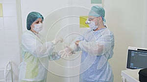Nurse helps a surgeon to put on sterile gloves before sclerotherapy surgery in hospital