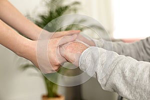 Nurse holding elderly man`s hands indoors, closeup. Assisting senior