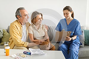 Nurse during home visit with senior couple, doctor holding clipboard in conversation with old man and woman