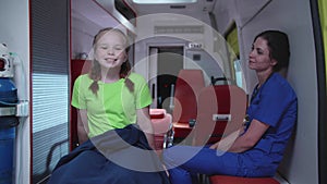 Nurse with little girl sit in ambulance car at night.