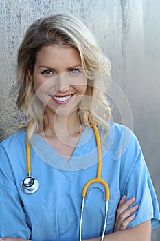 Nurse with long blonde hair and a stethoscope in a uniform smiling at the camera