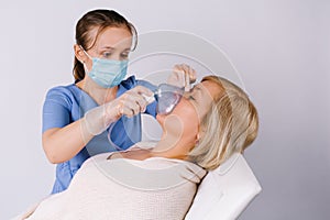 A nurse makes a nebulizer treatment for a Caucasian woman against respiratory diseases.