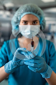 nurse in mask and gloves holding a syringe with medicine and waiting for a patient in surgery.