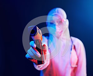 Nurse in mask and white uniform standing in neon lighted room and holding infrared thermometer. Stop coronavirus