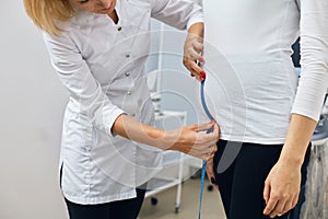Nurse is meassuring the height of the pregnant girl`s stomack photo