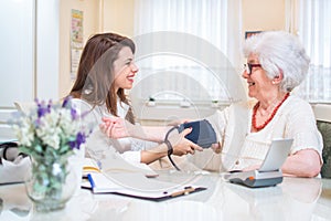 Nurse measuring blood pressure of senior woman at home.