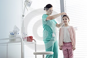 Nurse measuring height of girl against window at examination room