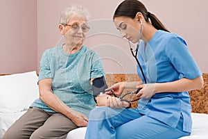 Nurse measuring senior woman`s blood pressure in hospital ward