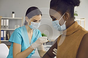 Nurse in medical face mask giving injection to patient during vaccination campaign