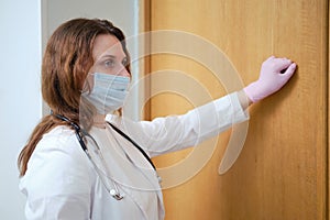 Nurse in medical mask knocking on the door of the house. Concept of problems during the coronavirus epidemic photo